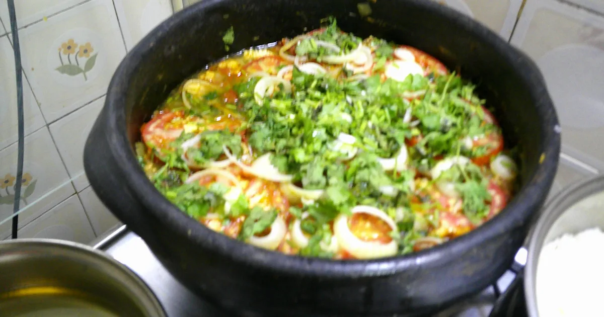 Moqueca capixaba sendo preparada na panela de barro, com tomate, cebola e coentro