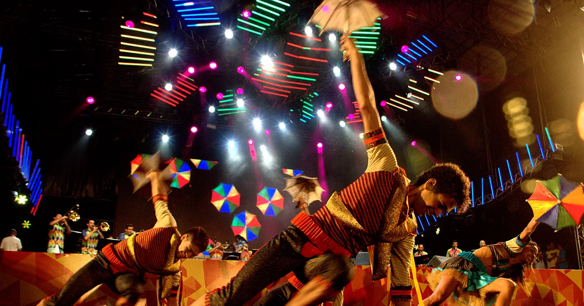 Passistas de frevo dançando com sombrinhas coloridas em um palco iluminado durante o Carnaval