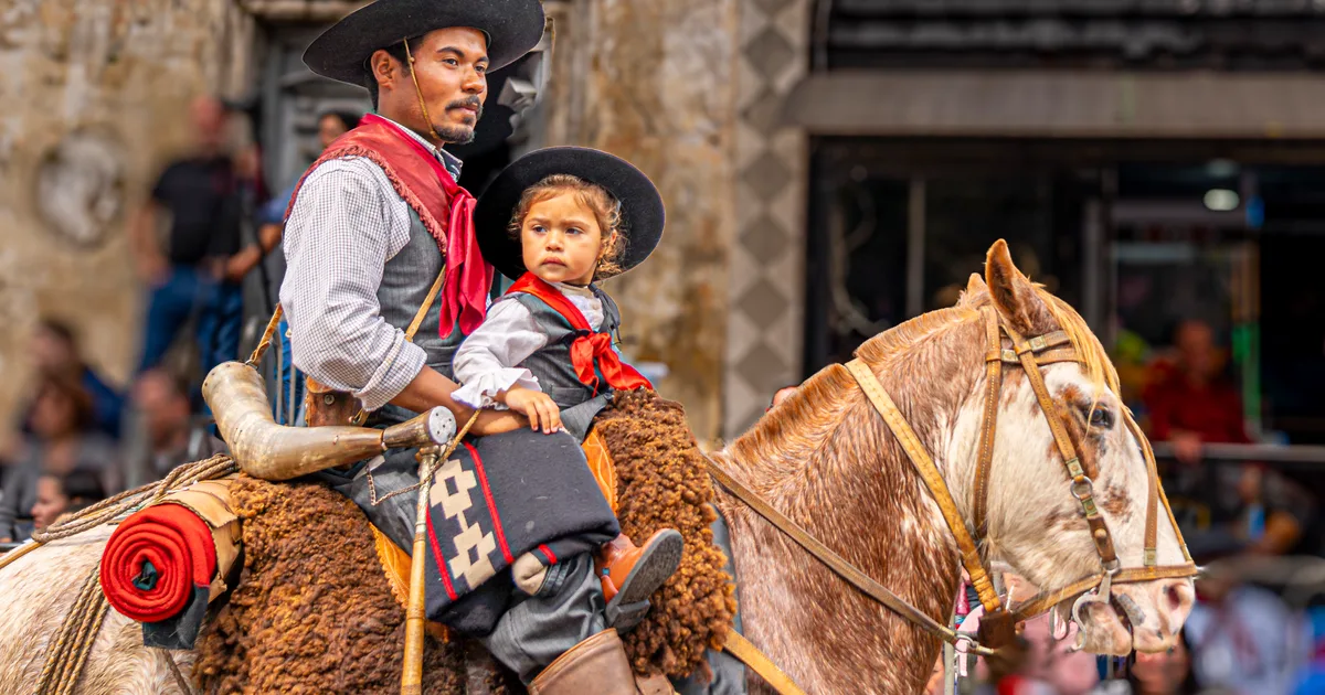 Gaúcho e criança a cavalo, em trajes de pilcha, durante desfile da tradição gaúcha